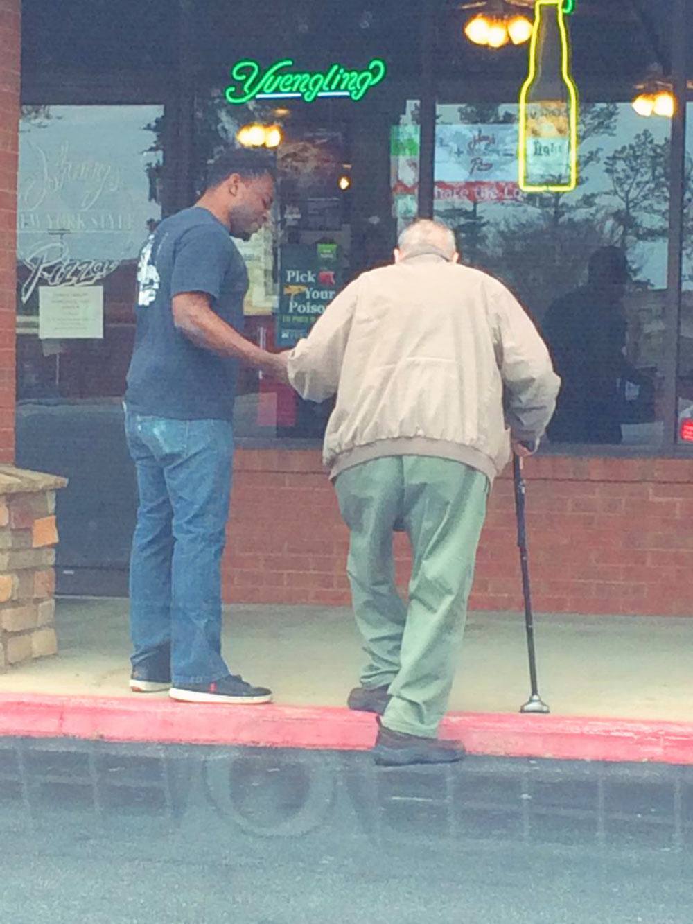 Photo shows Johnny’s New York Style Pizza employee helping elderly man cross the street.